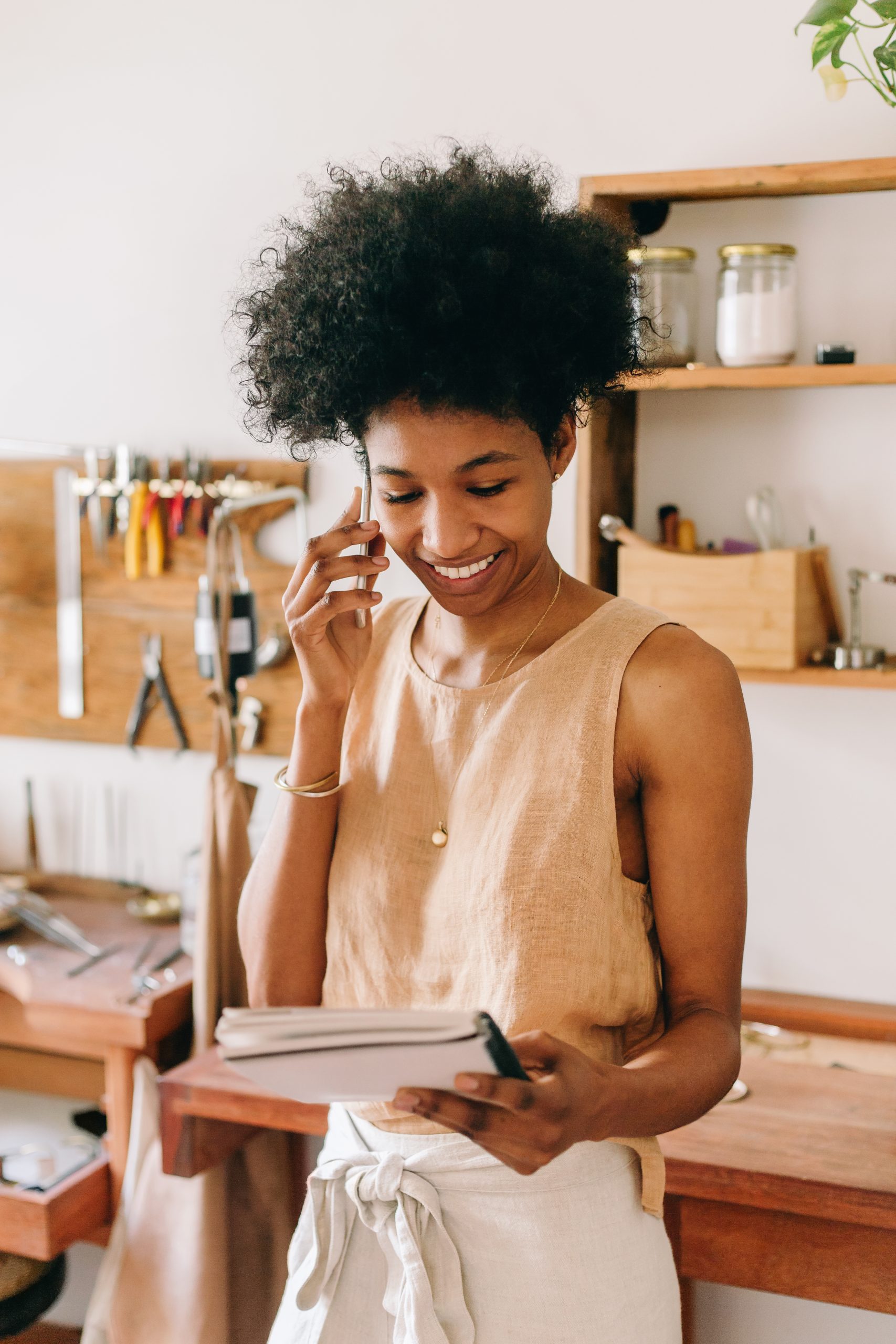 Accessories entrepreneur discussing commissioned order details on phone in studio, with workshop tools visible in the background.